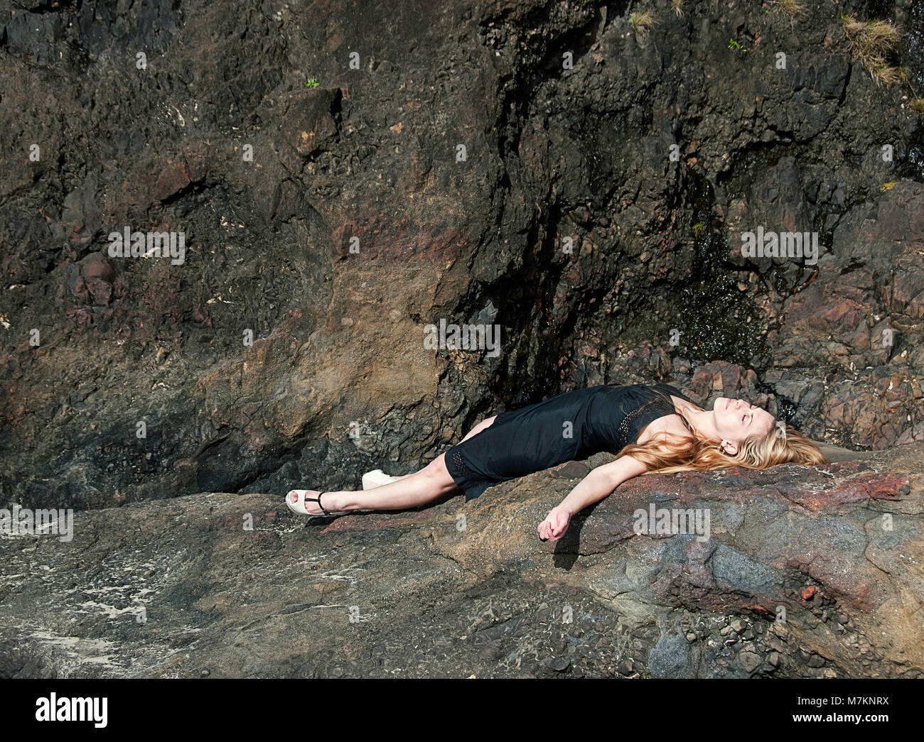 Une femme allongée sur un rocher côtier porter des chaussures à talons hauts. Banque D'Images