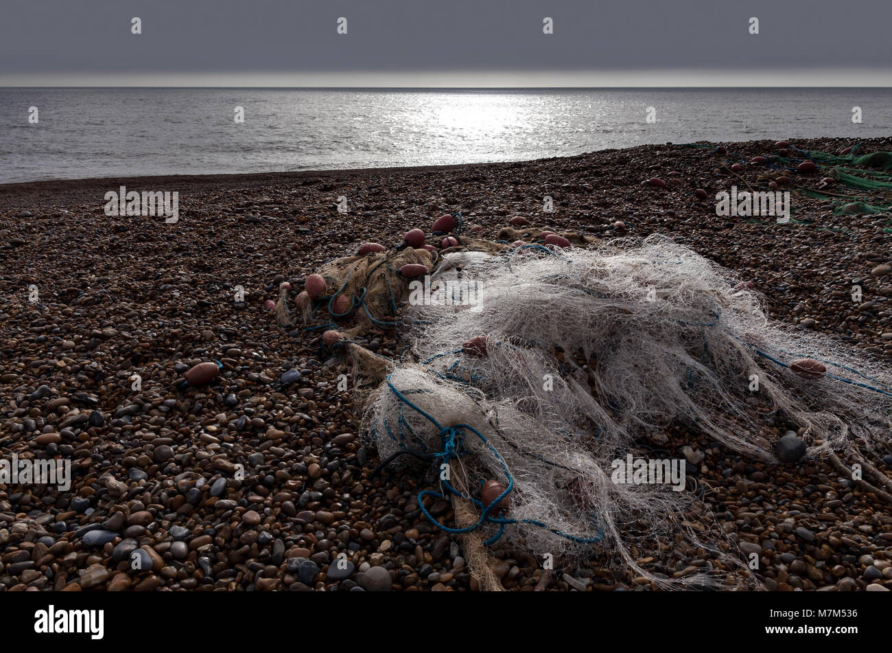 Filet de pêche en nylon dans un tas sur une plage de galets avec la mer en arrière-plan et la lumière diffusée sur le net scintillants Banque D'Images