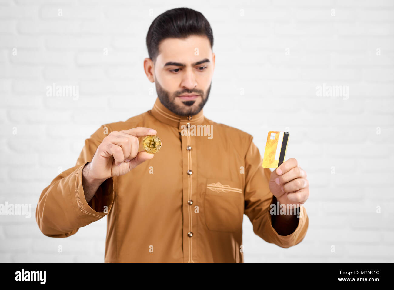 Beau être sérieux musulman pendant la recherche de carte de crédit et holding bitcoin or Banque D'Images