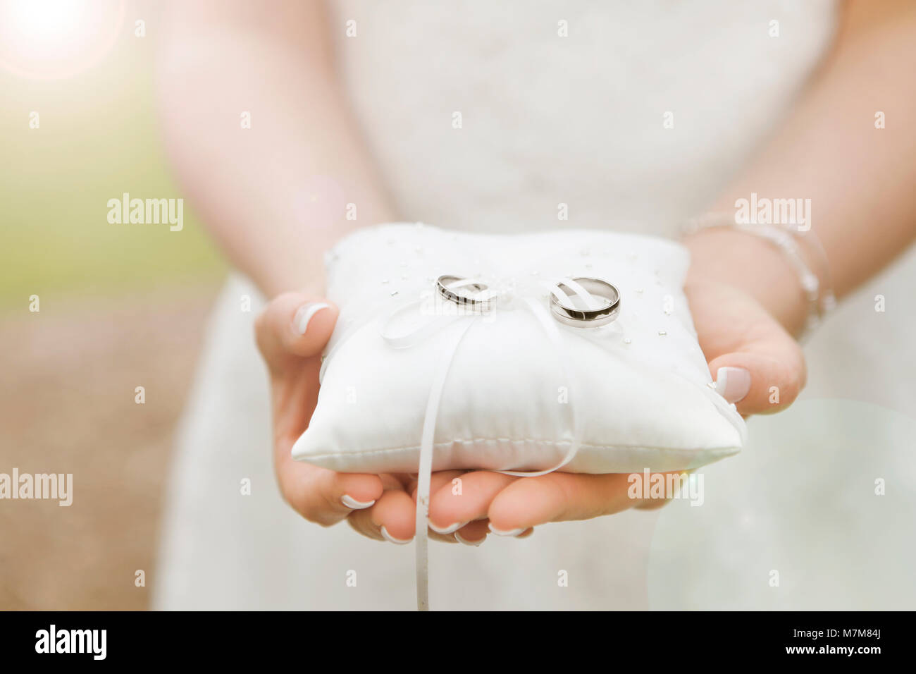 Une épouse est titulaire d'un coussin avec les nouveaux anneaux de mariage dans ses mains Banque D'Images