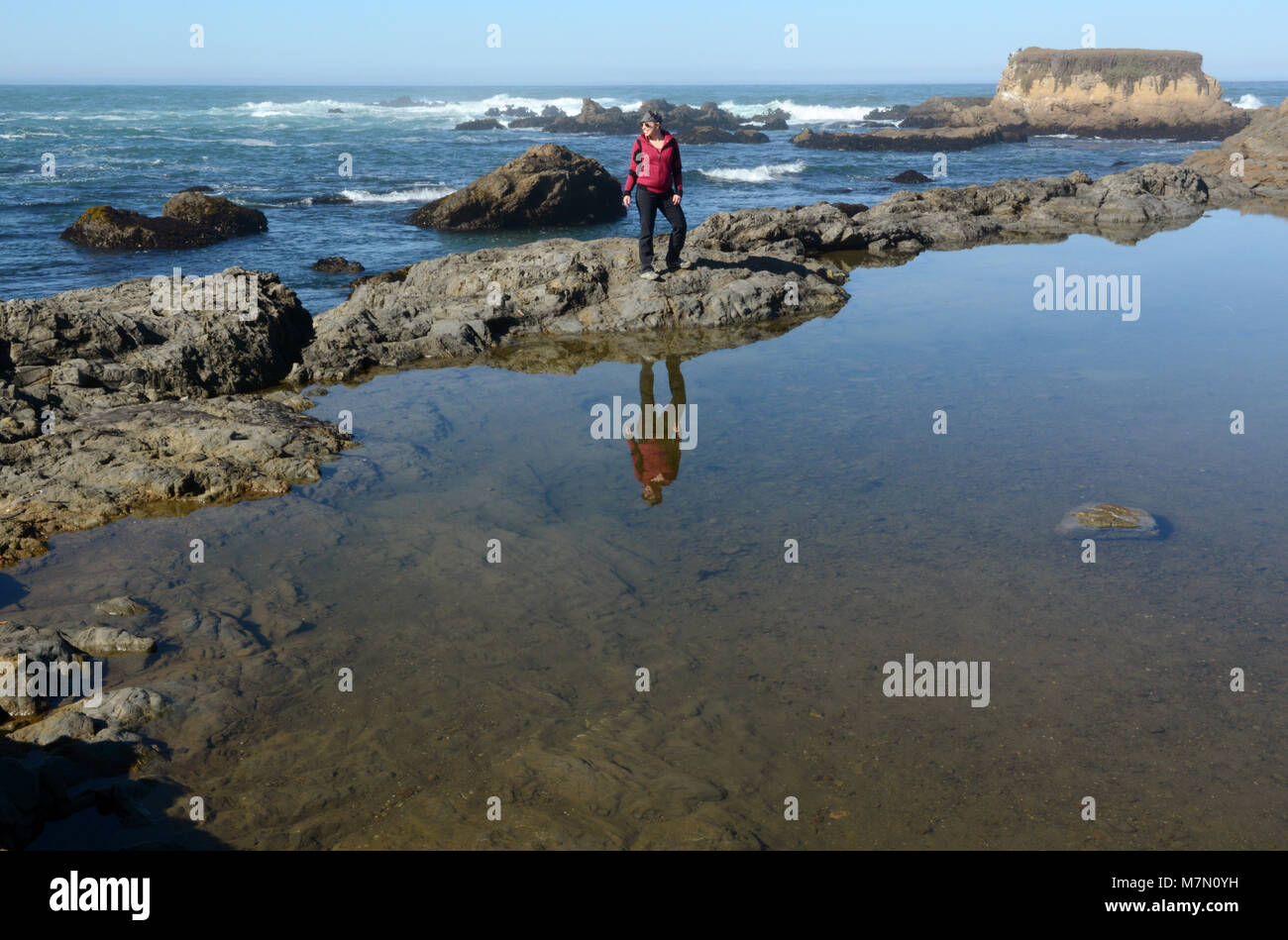 Une femme se tient sur des roches dans l'océan. Elle est à la recherche vers la côte tout en souriant. Banque D'Images