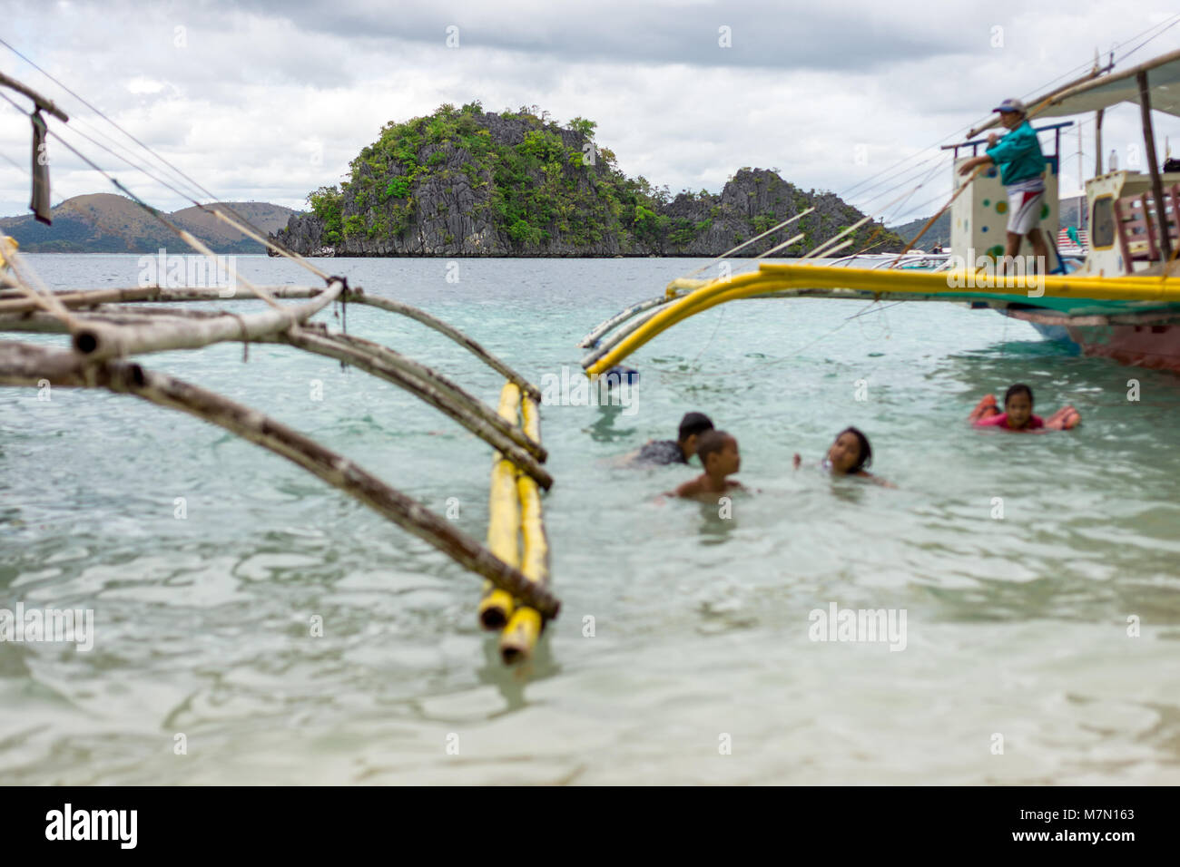 Les enfants philippins jouant dans la mer autour de l'tangons de bateaux de pêche traditionnelle locale typique avec petite île de roche. Banque D'Images