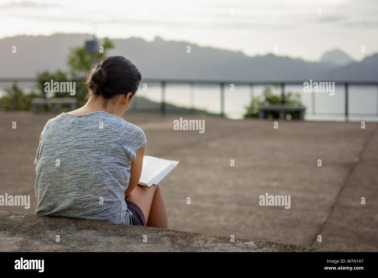 Une jeune femme se concentre de lire ici le dos dur livre tout en s'assit sur des mesures concrètes. Banque D'Images