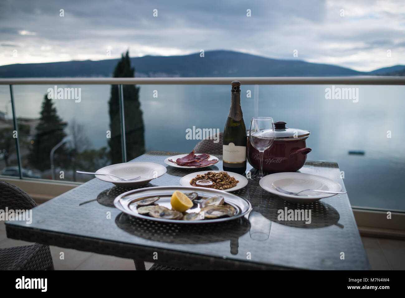 Table avec des aliments locaux et du vin à l'accueil balcon. Se concentrer sur la bouteille. Arrière-plan de la mer et les montagnes. Les huîtres avec du citron, de la viande, des en-cas. Still Life Banque D'Images