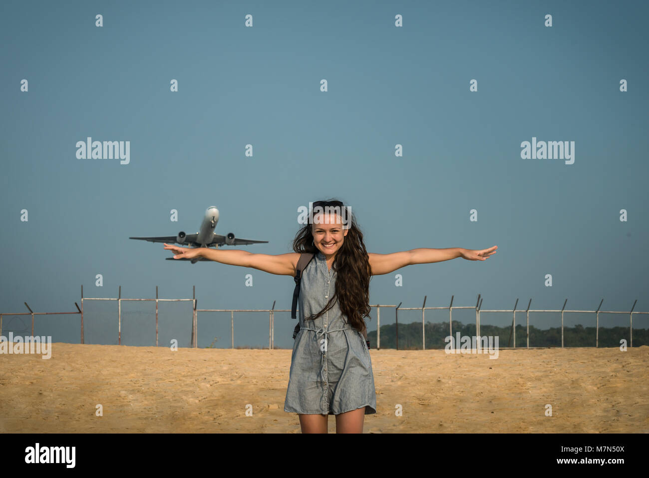 Jet avion décolle sur l'arrière-plan derrière une jeune femme. La femme est debout et posant sur la plage près de l'aéroport et la propagation des armes prêtes pour flyaway. Banque D'Images
