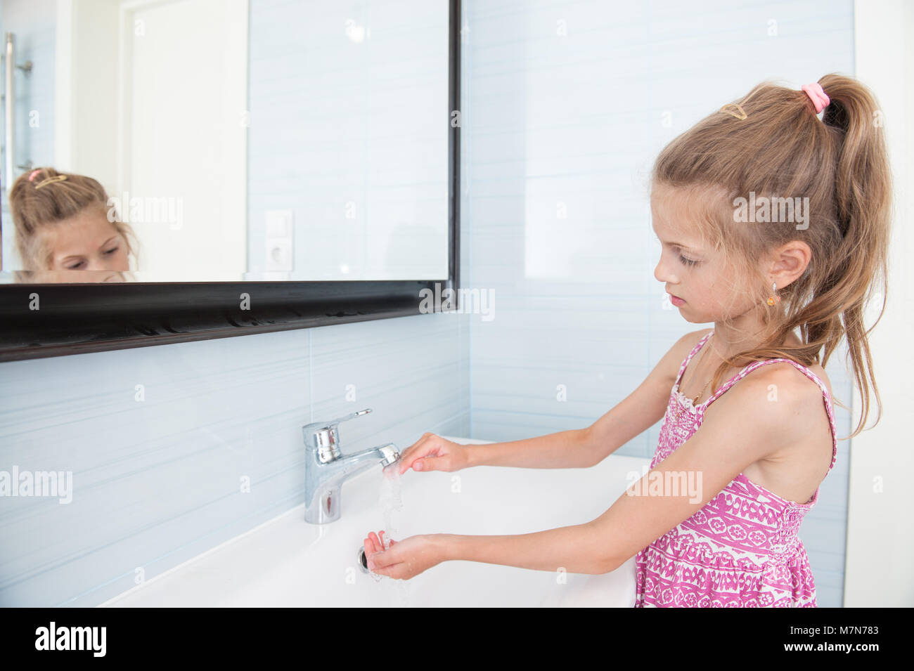 Petite fille en robe se lave les mains dans le lavabo dans la salle de bains Banque D'Images