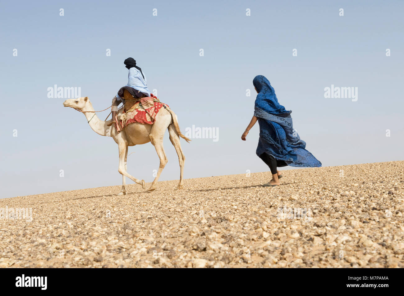 Femme marchant derrière un homme monté sur un chameau en Mauritanie,Western Sahara. Banque D'Images