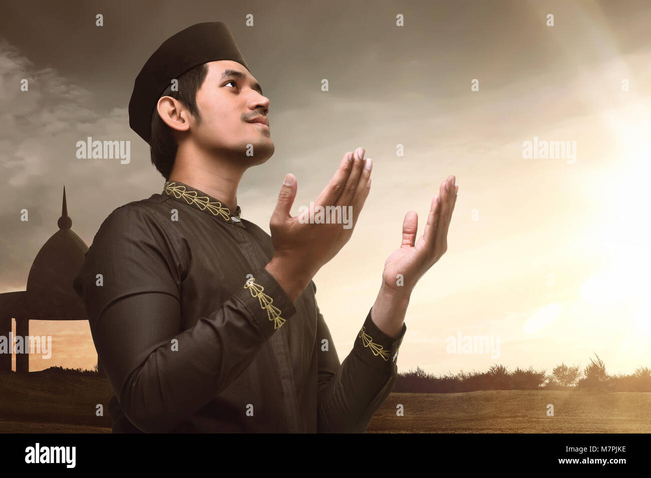 Jeune asiatique musulman raising hand et priant avec fond coucher de soleil Banque D'Images