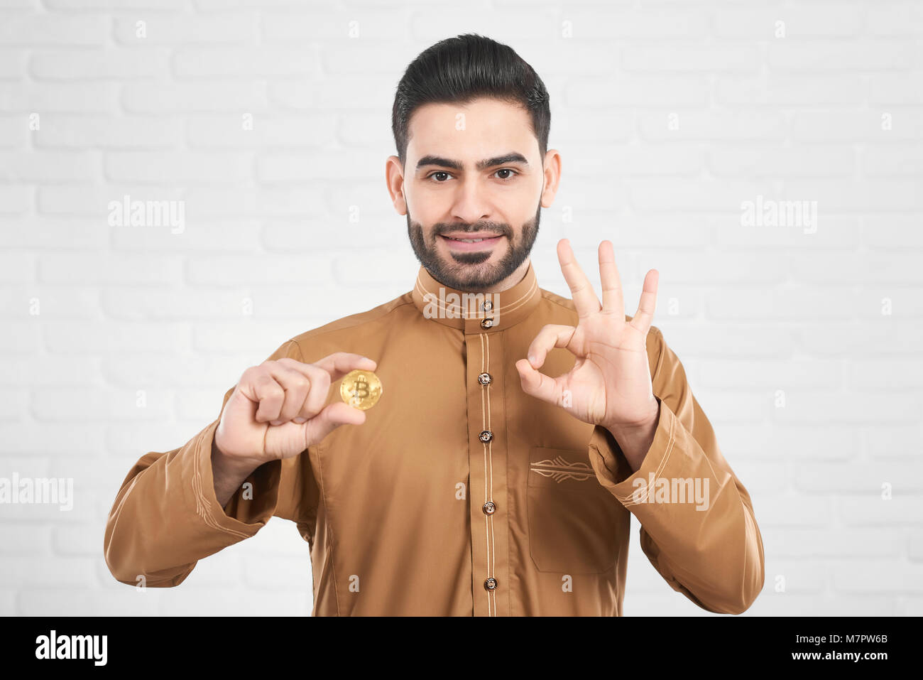 Investissement réussi de beau mâle modèle islamique et bitcoin or holding montrant ok sign Banque D'Images