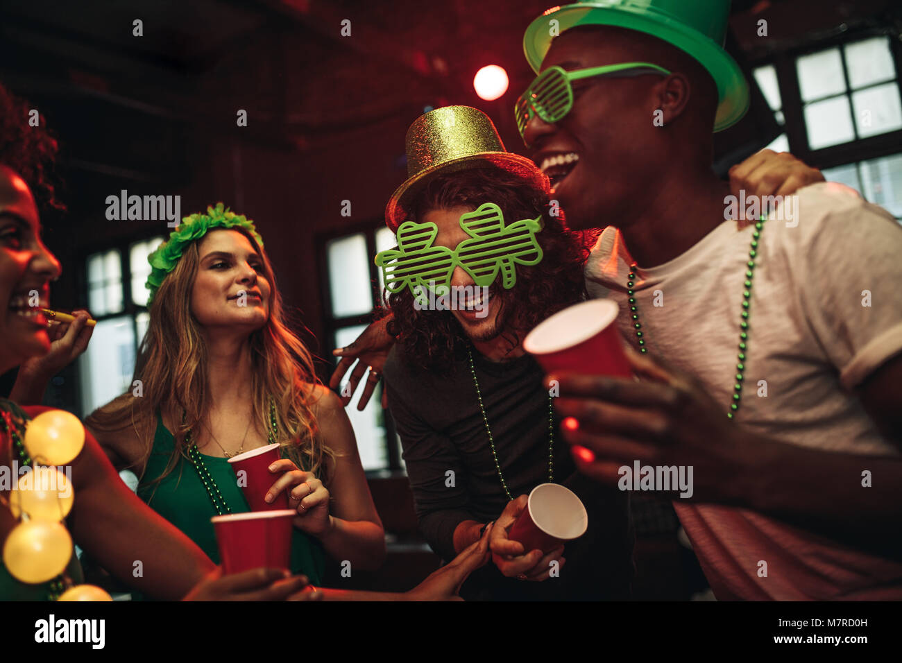 Groupe de jeunes hommes et de la femme pour célébrer la Saint-Patrick. Les amis de s'amuser au bar avec le parti vert lunettes et chapeau. Banque D'Images