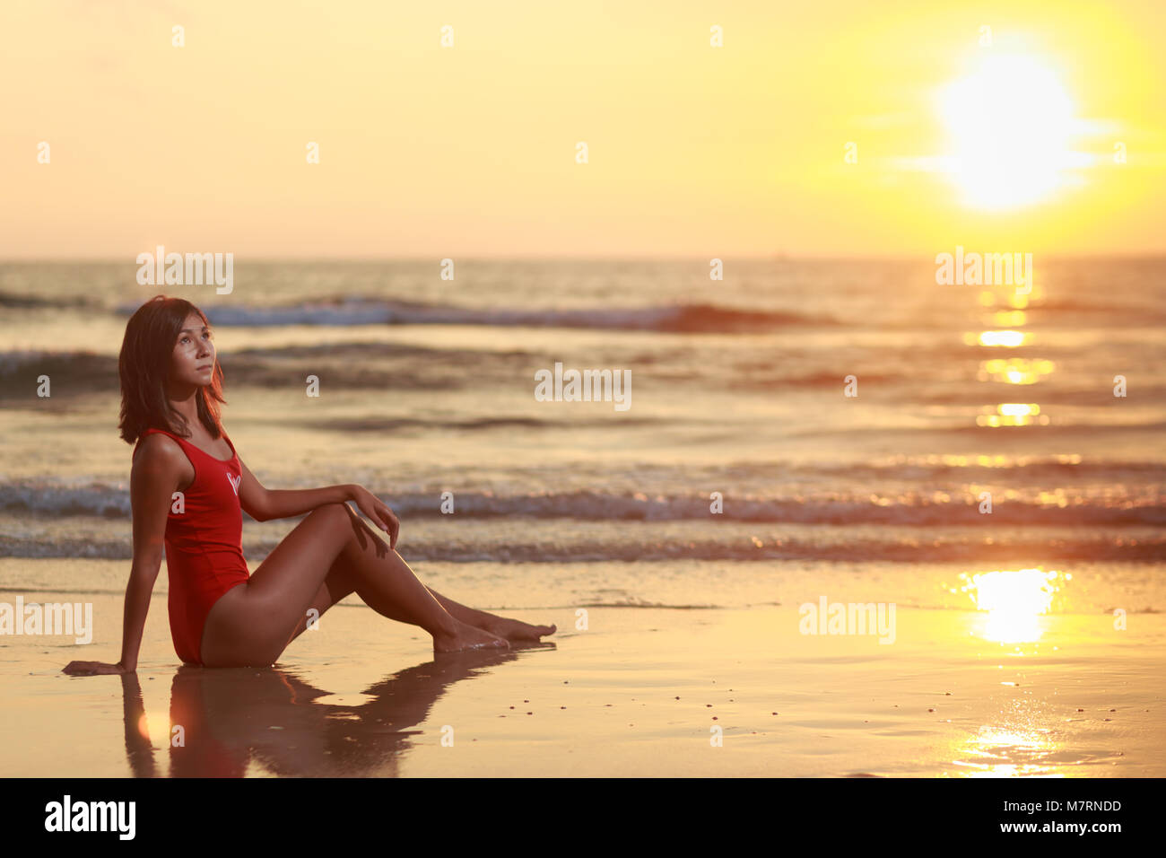 Beau modèle féminin bras ouverts sous le lever du soleil au bord de mer. Soleil est sous l'horizon. Girl est seul dans l'eau Banque D'Images
