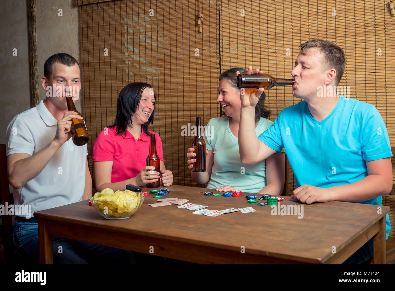 Une compagnie d'amis de boire une bière et jouer aux cartes assis à une table à l'intérieur Banque D'Images