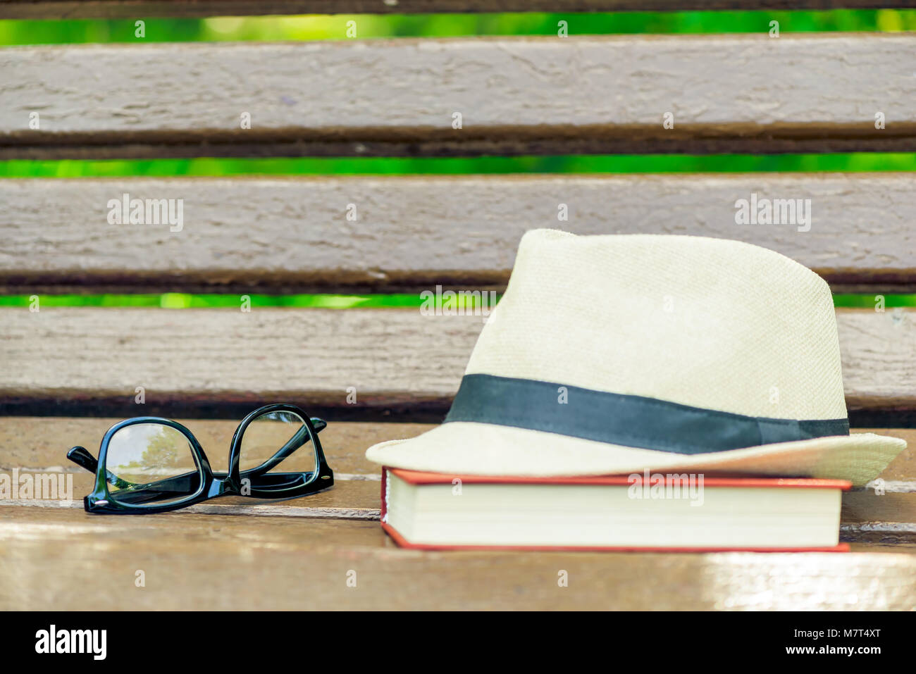 Chapeau de paille, lunettes et un livre épais sur un banc en bois dans le parc Banque D'Images