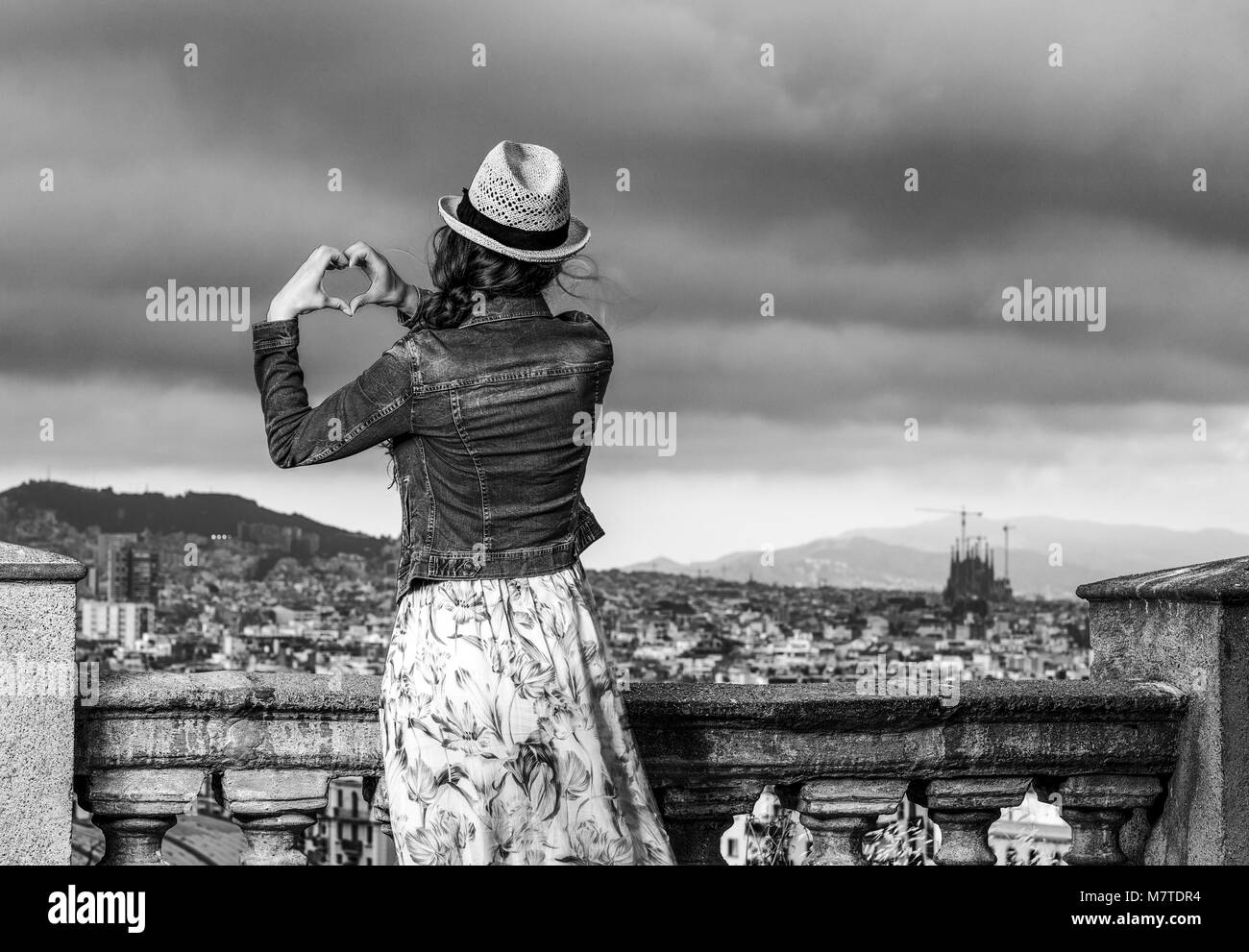 Soirée parfaite avec vue magnifique. Vus de derrière, voyageur élégant femme en robe et chapeau de paille à Barcelone, Espagne montrant la main en forme de coeur Banque D'Images