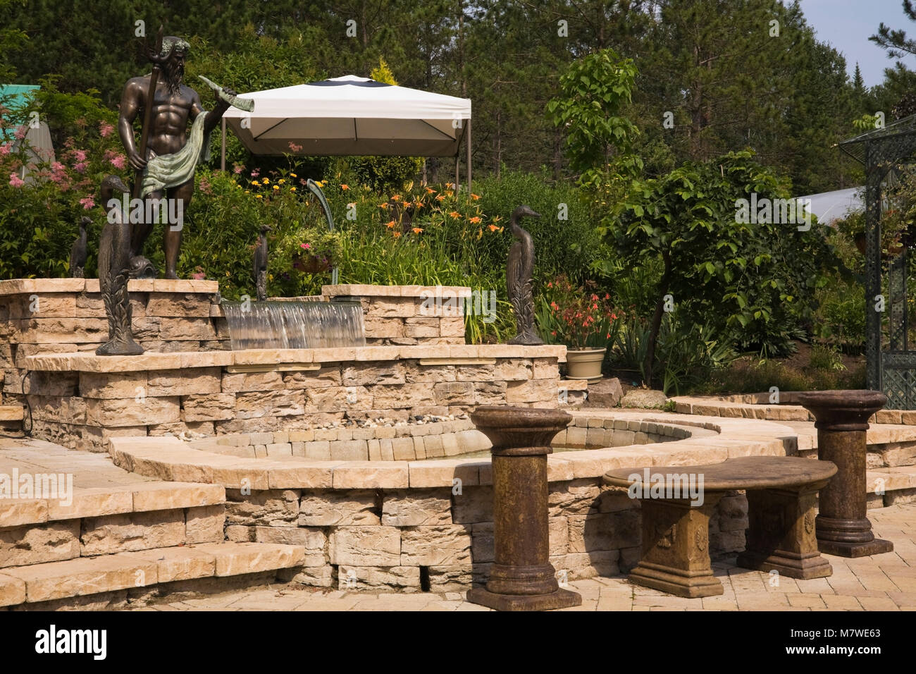 Light Brown Dalle patio avec fontaine d'eau en cascade et le ciment teinté et statues de bronze dans le jardin en été Banque D'Images