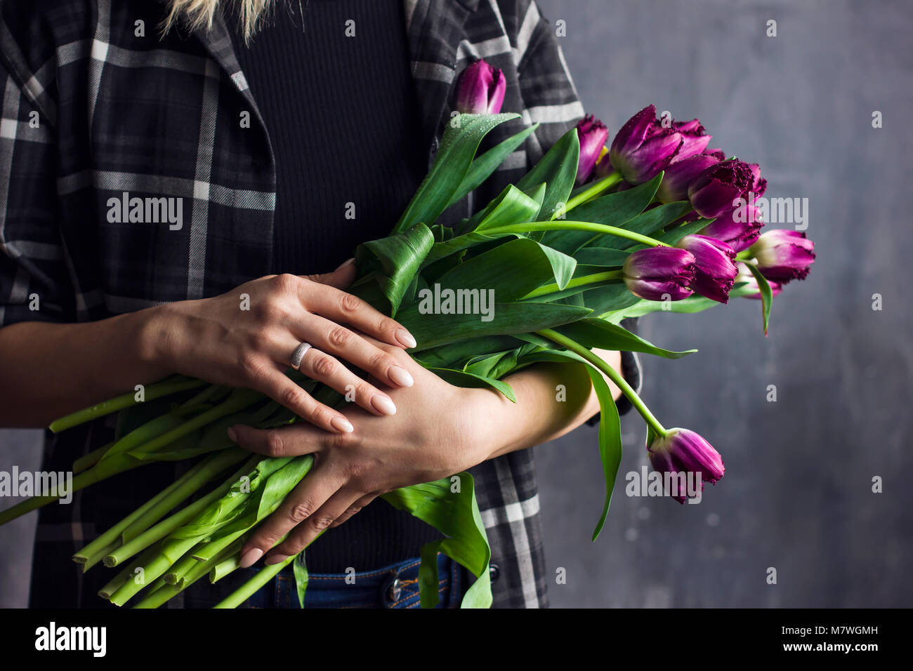 Jeune femme en chemise à carreaux holding bouquet de tulipes, terry violet fond sombre Banque D'Images