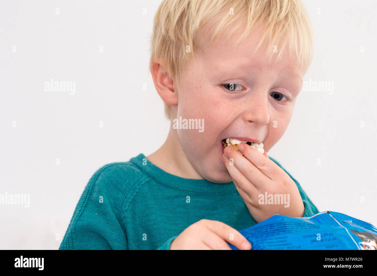 Didim, Turquie - 01 octobre 2017 : Sweet garçon blond aux yeux bleus de manger un sac de popcorn devant un fond blanc. Banque D'Images