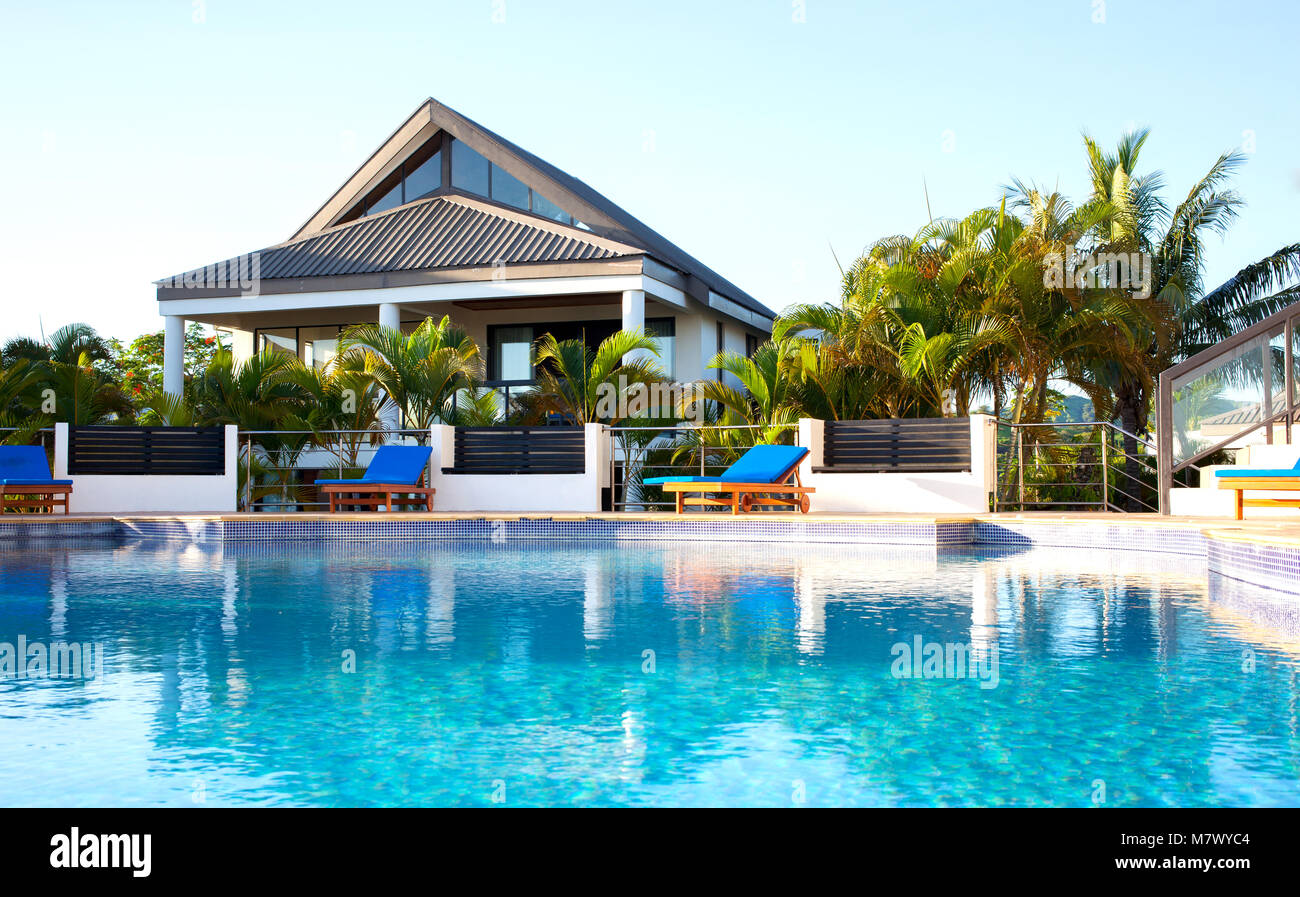Avis de villa de luxe avec piscine entourée de palmiers et de sièges aux Fidji pendant belle journée ensoleillée et chaude. Banque D'Images