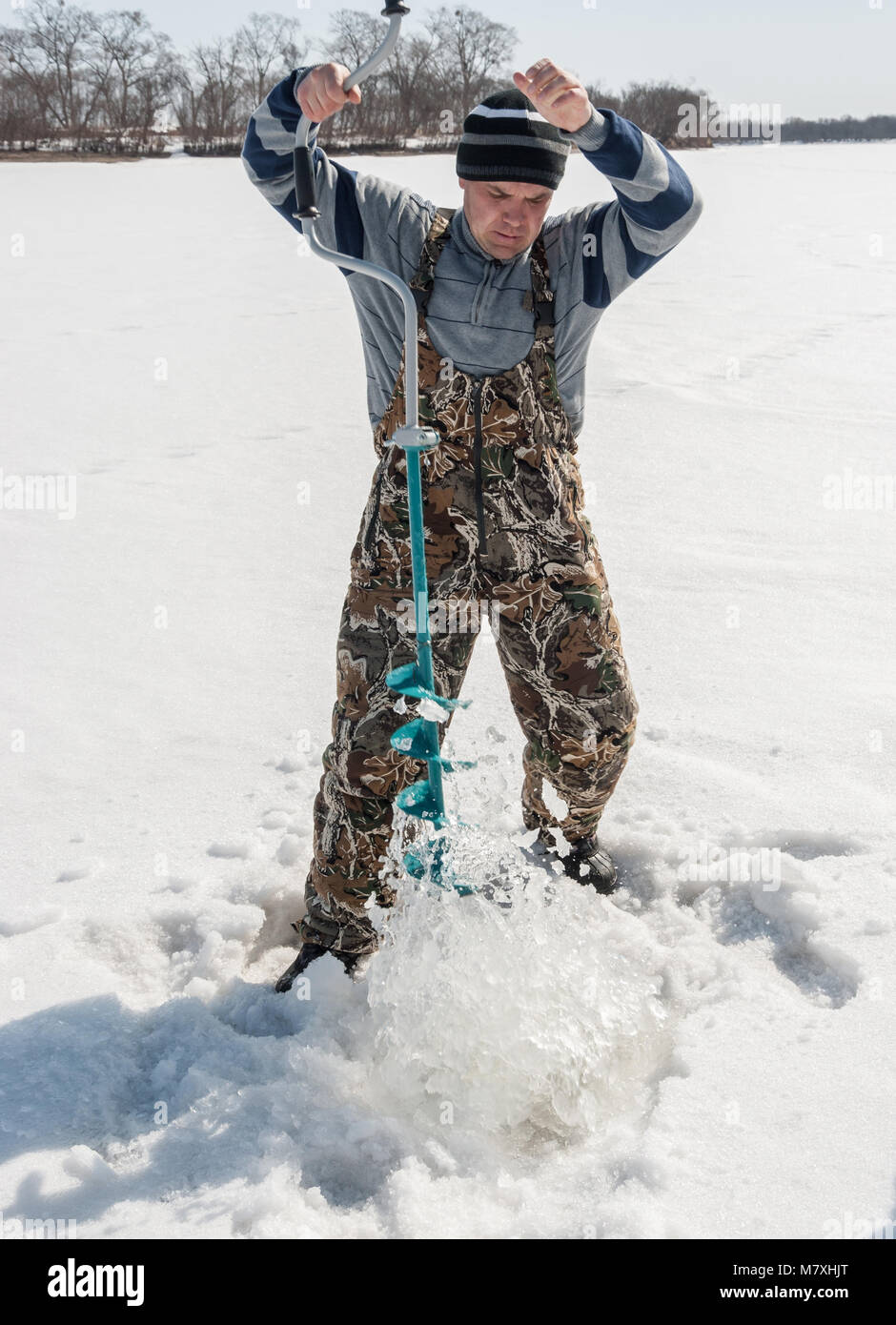 La pêche d'hiver sur la rivière. Jeune homme percer un trou dans la glace. Banque D'Images