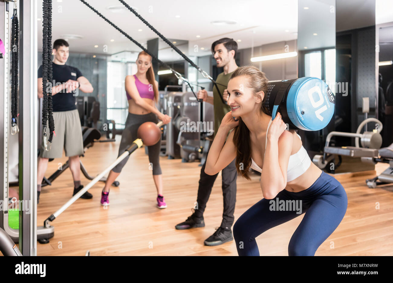 Jeune femme fit faire l'exercice s'accroupit tout en tenant un sac lourd Banque D'Images