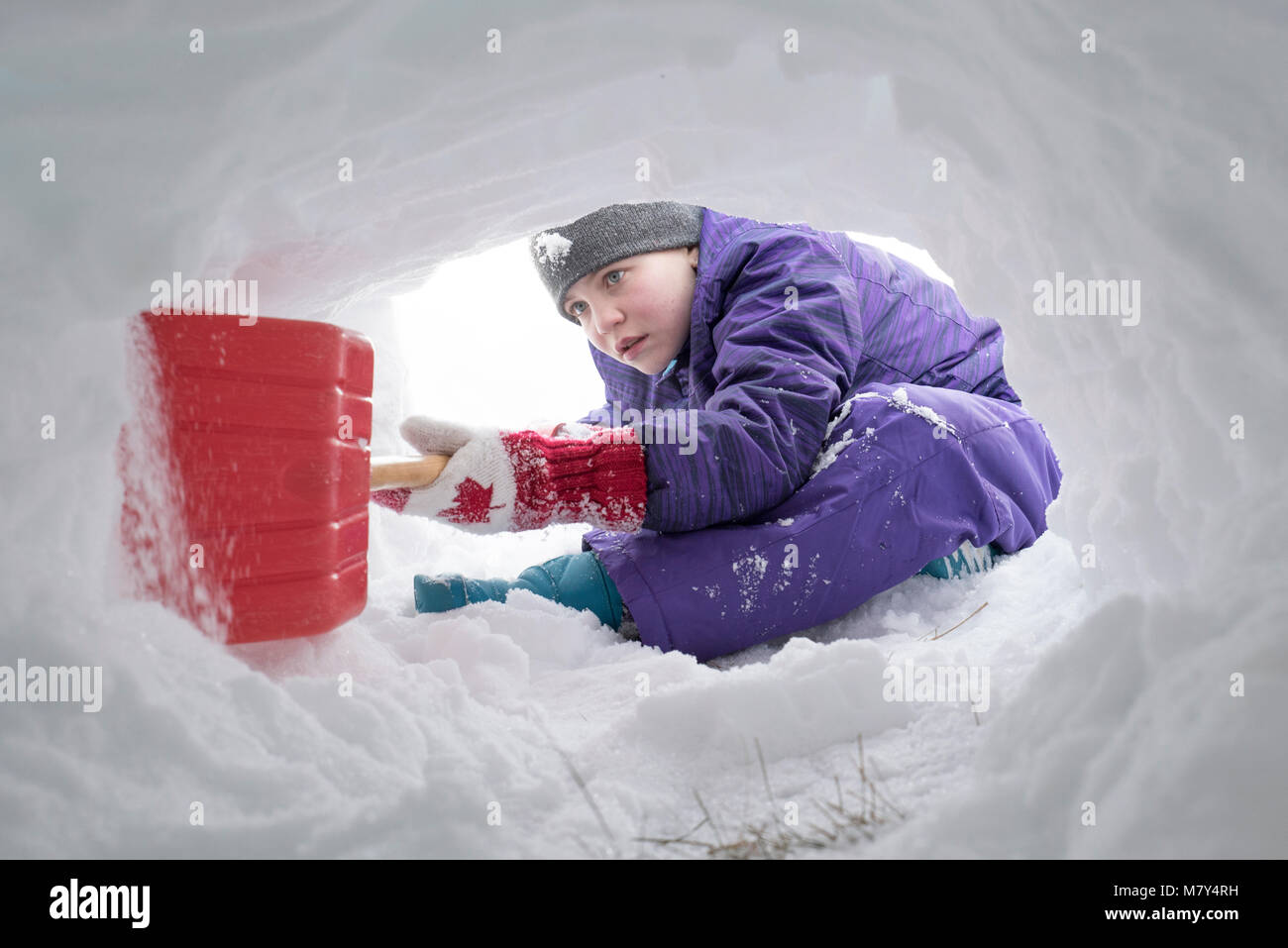 Jeune canadienne à creuser le tunnel de la neige avec une pelle en plastique rouge Banque D'Images