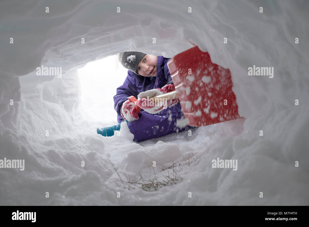 Jeune canadienne à creuser le tunnel de la neige avec une pelle en plastique rouge Banque D'Images