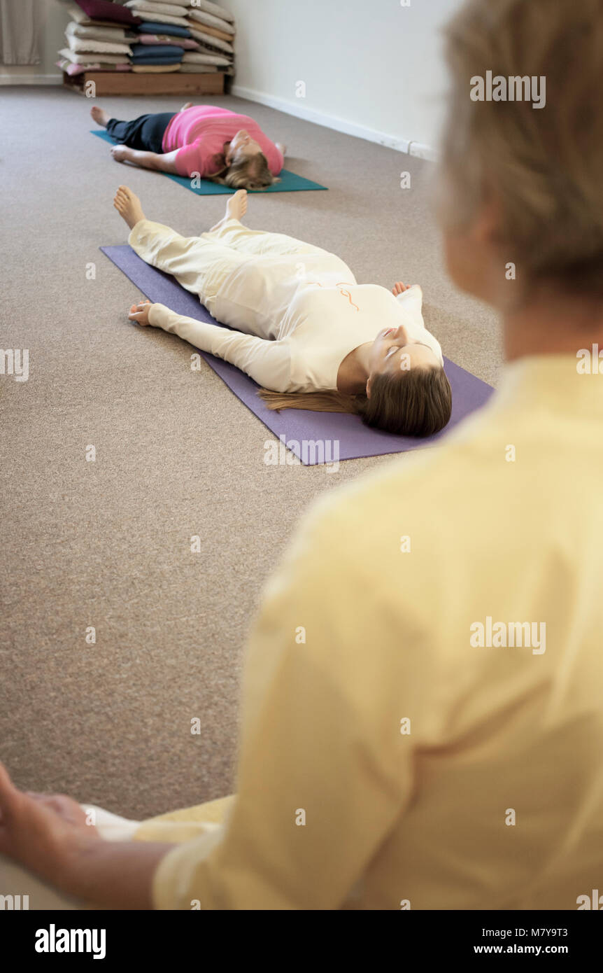 Les jeunes gens pratiquant également appelée relaxation yoga nidra. Guidé par un instructeur certifié de yoga femme pose en shavasana sur theri dos on yoga mat Banque D'Images