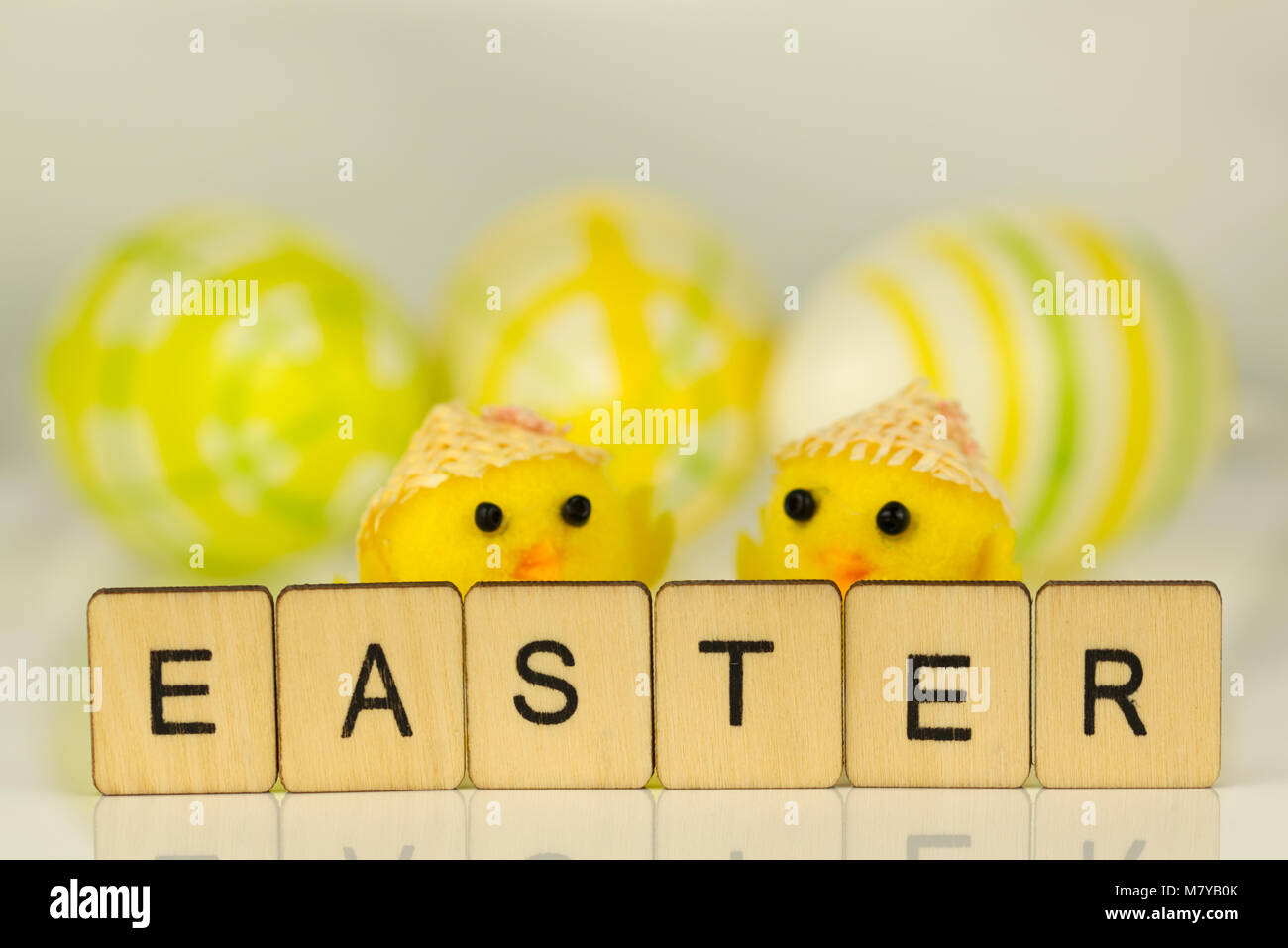 Le mot Easter écrit en lettres sur la surface blanche réfléchissante jaune avec des poussins et des oeufs peints hors focus à l'arrière-plan. Banque D'Images