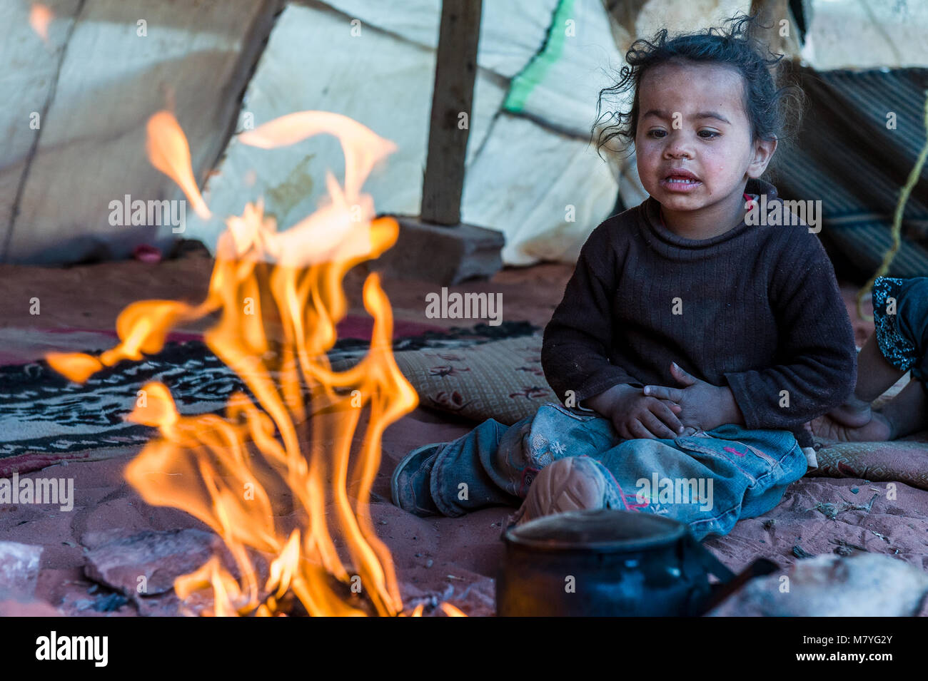 Jeune fille bédouine regardant l'incendie dans une tente miteuse dans le Wadi Rum, Jordanie. Banque D'Images