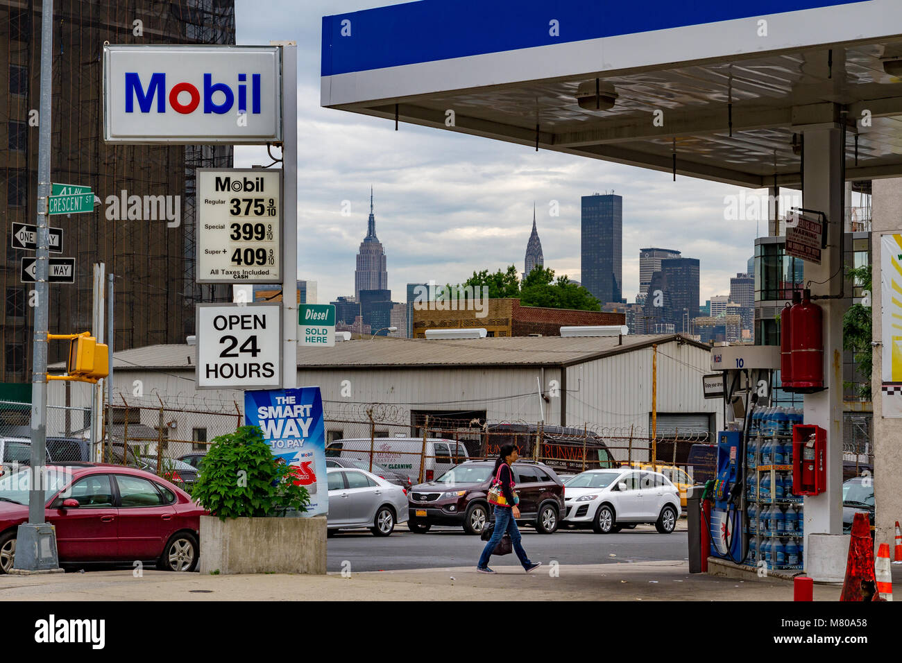 Une femme traverse la piste d'une station-service de Mobil Gas / station-service à long Island City, Queens, New York Banque D'Images