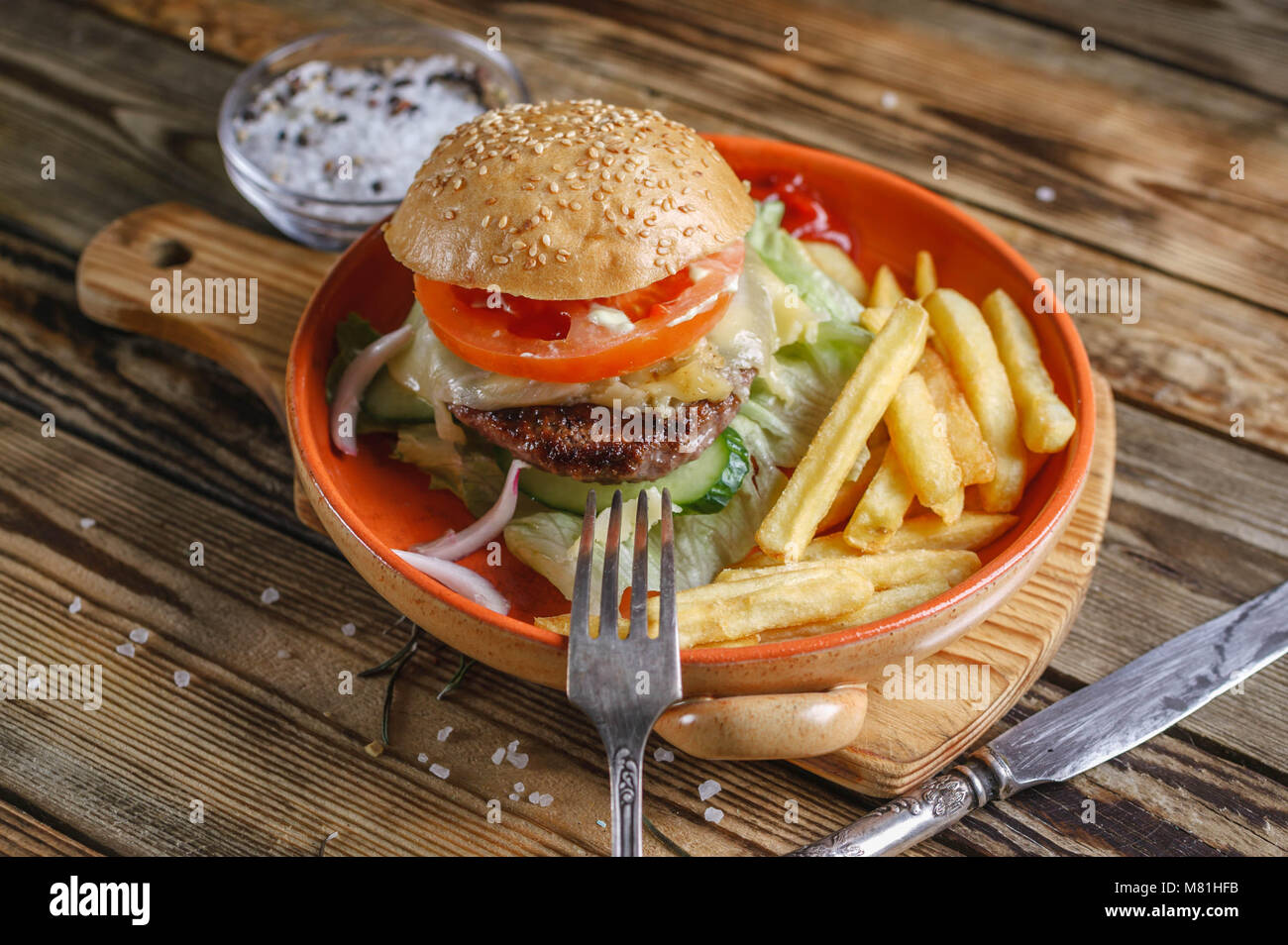 Home-made hamburger au boeuf, tomate et salade sur une plaque avec des pommes de terre rissolées. Fond de bois Banque D'Images