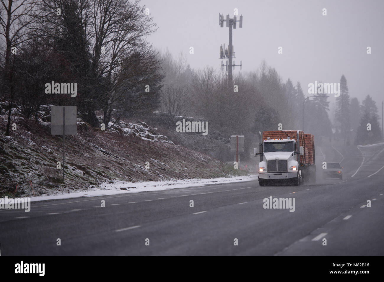 Big Rig bonnet blanc américain day cab semi truck le transport du bois d'œuvre sur une semi-remorque et la conduite sur autoroute en hiver par temps de neige Banque D'Images