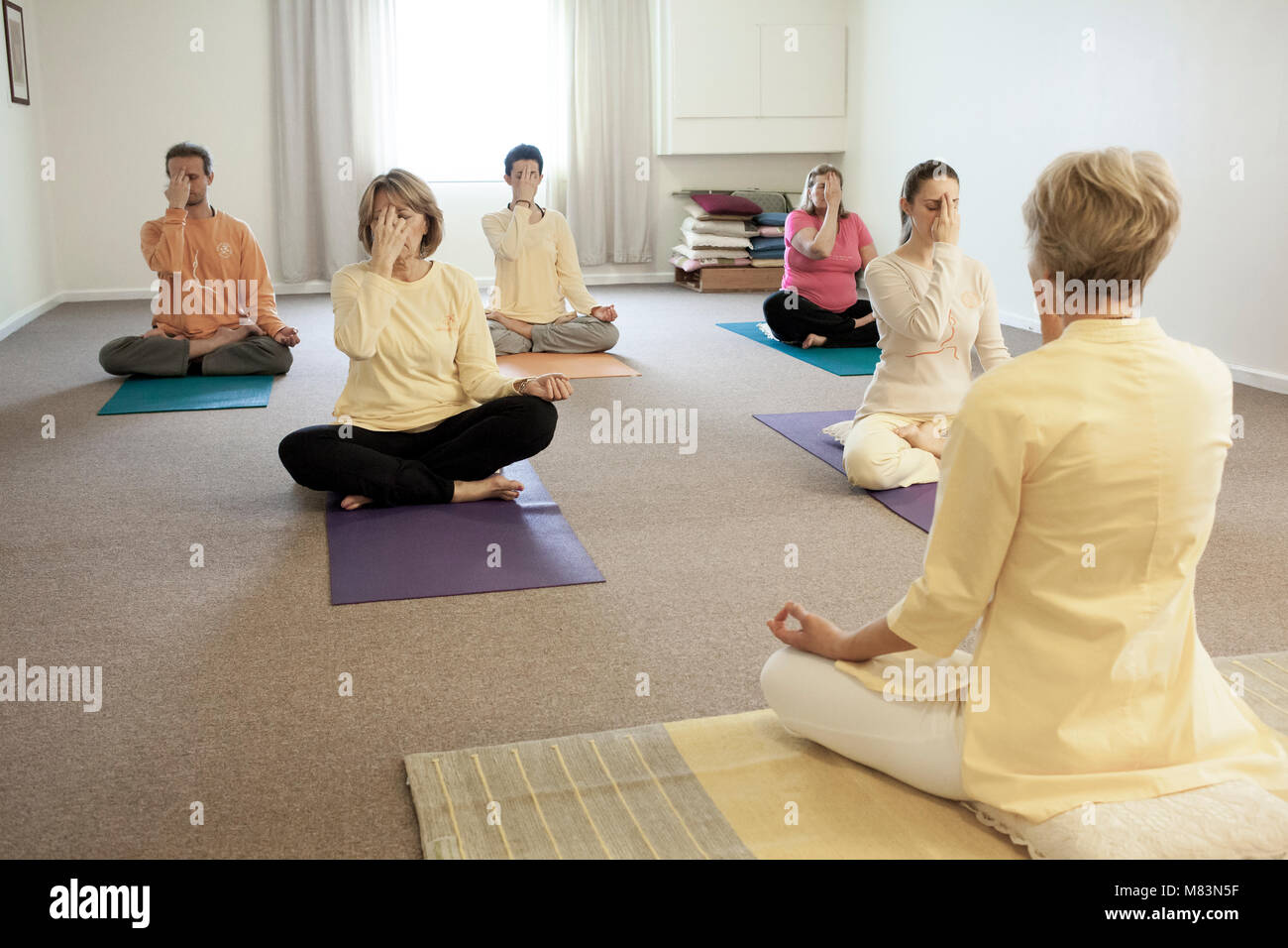 Un groupe de personnes pratiquant la respiration yogique technique appelée Pranayama, assis avec les jambes croisées, dos droit, les yeux clos, la main gauche reposant sur t Banque D'Images