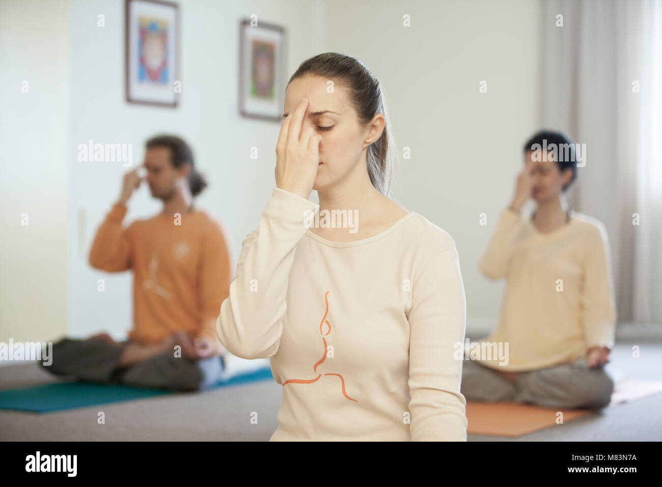 Un groupe de jeunes pratiquant la respiration yogique technique appelée Pranayama, assis avec les jambes croisées, dos droit, les yeux fermés, main gauche restin Banque D'Images