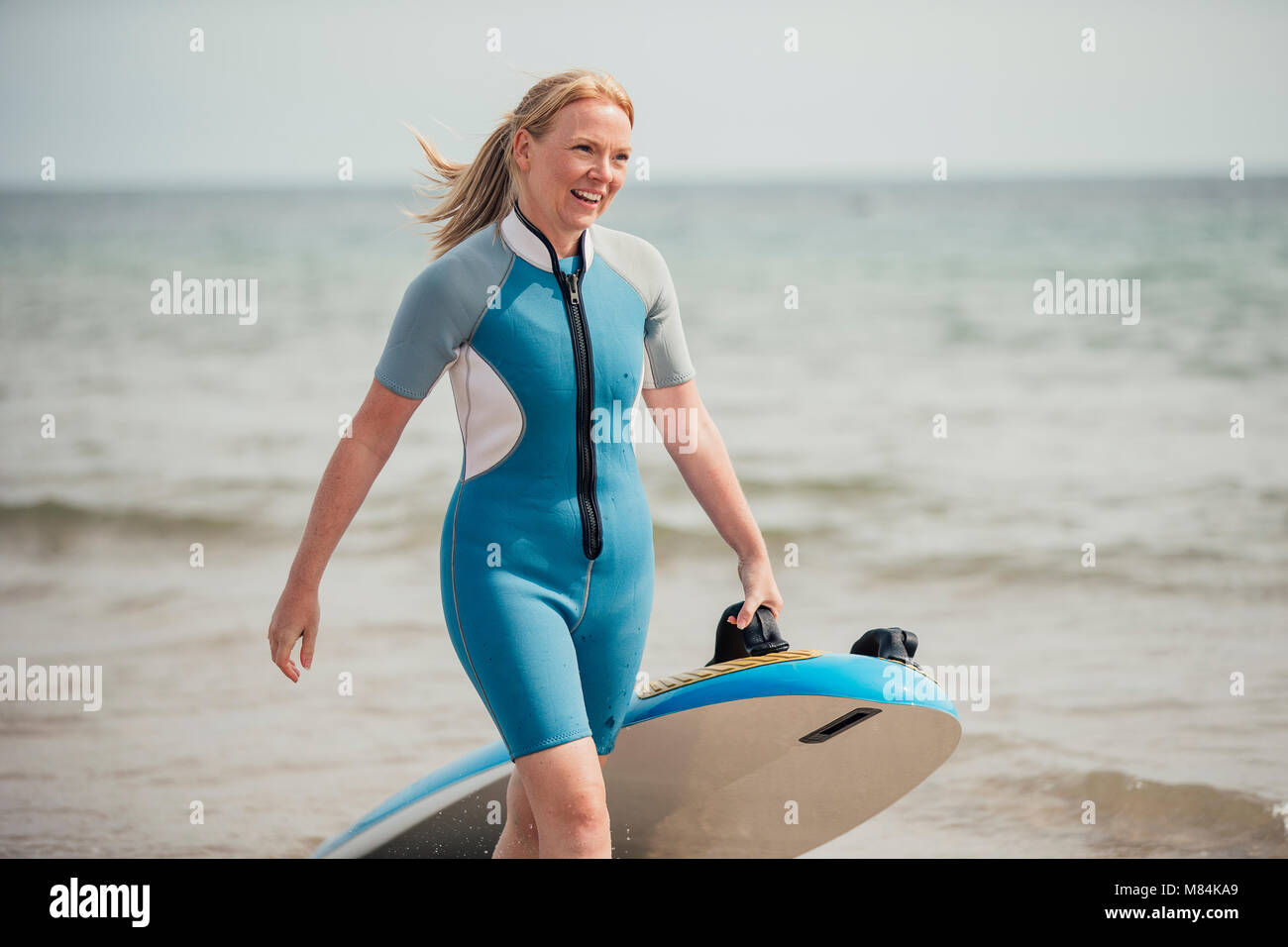 La femme est de retour d'une session de surf à la plage. Elle tire une planche de surf. Banque D'Images