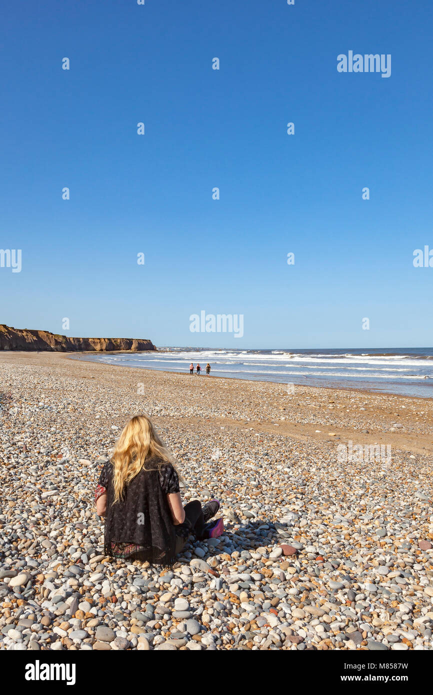 Une femme assise sur la plage à Seaham, County Durham, vers Sunderland. à la fin de l'été soleil et examine sea glass trouvés parmi les cailloux, UK Banque D'Images