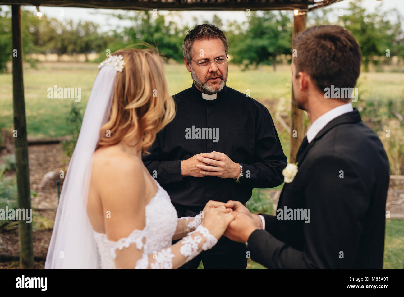 Le prêtre masculin épouse un couple dans une belle cérémonie de mariage en plein air. cérémonie de mariage d'un couple élégant tenant la main et prenant des vœux. Banque D'Images Le prêtre masculin épouse un couple dans une belle cérémonie de mariage en plein air. cérémonie de mariage d'un couple élégant tenant la main et prenant des vœux. Banque D'Images