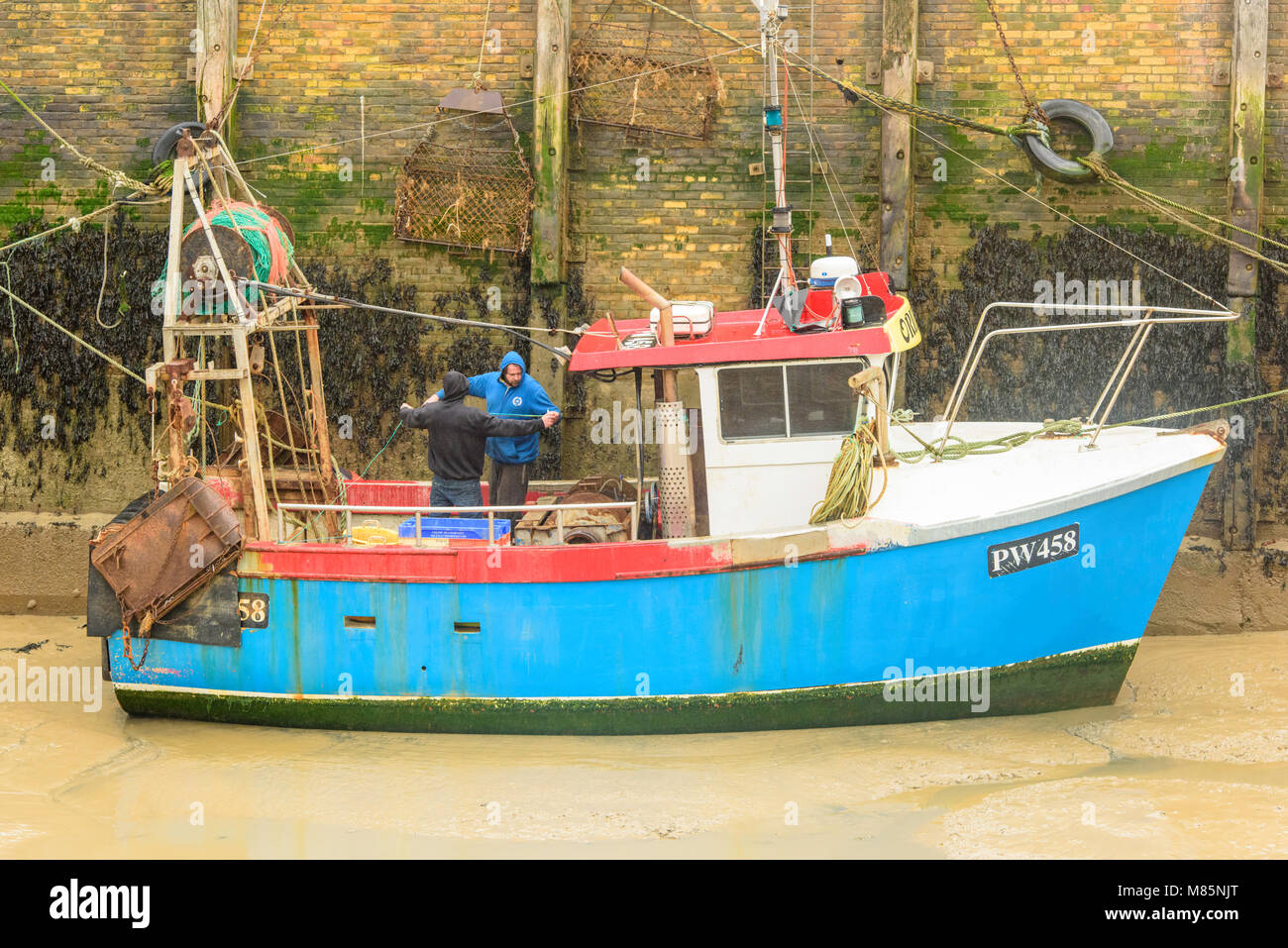 Deux pêcheurs travaillant sur le pont d'un bateau de pêche dans le port de Whitstable, Kent, à marée basse. Banque D'Images