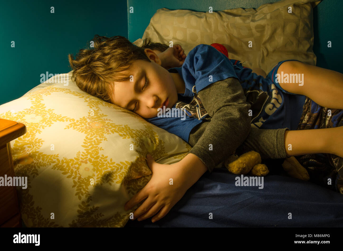Deux jeunes frères endormis dans le même lit à la nuit. La scène est éclairée par la lueur d'une lampe de chevet. Banque D'Images
