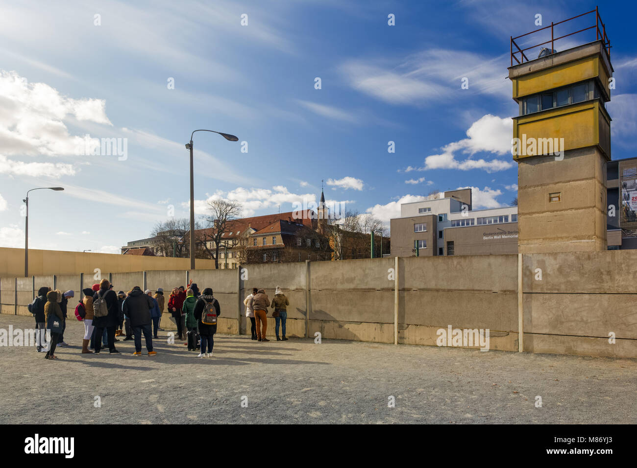 Groupe de touristes debout devant les vestiges du mur de Berlin (Berliner mauer) Berlin, Allemagne. Une ancienne tour de sécurité est vue au coin de la rue Banque D'Images