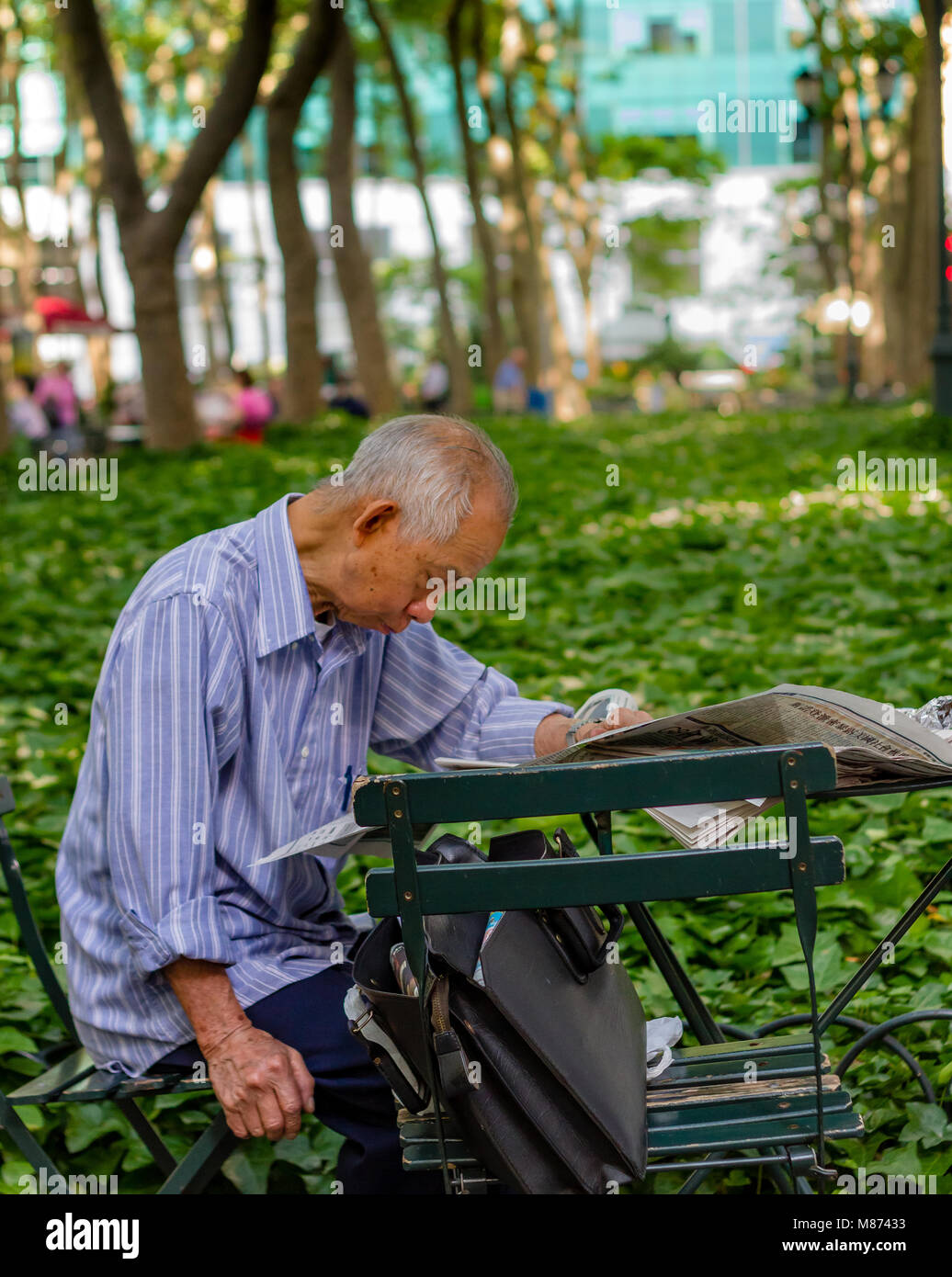 Un chinois de s'asseoir à une table de lire le journal dans Bryant Park, Manhattan, New York City Banque D'Images