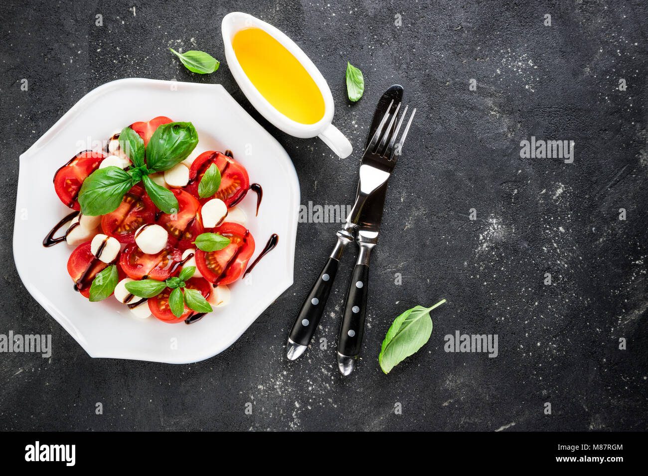 Salade Caprese. Tomates, mozzarella, tomates, huile d'olive, Basilic Feuilles d'herbes, sauce balsamique sur fond sombre. Cuisine italienne. Vue d'en haut Banque D'Images