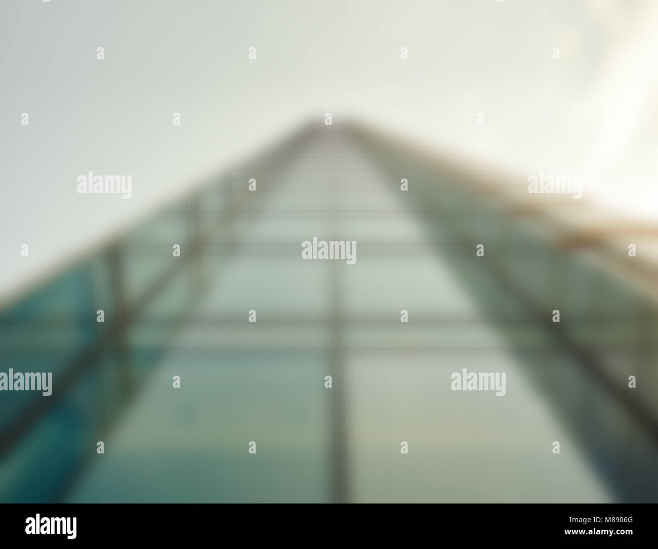 Defocused low angle droit d'un gratte-ciel moderne en verre s'élevant jusqu'au ciel dans le quartier commerçant d'une ville Banque D'Images