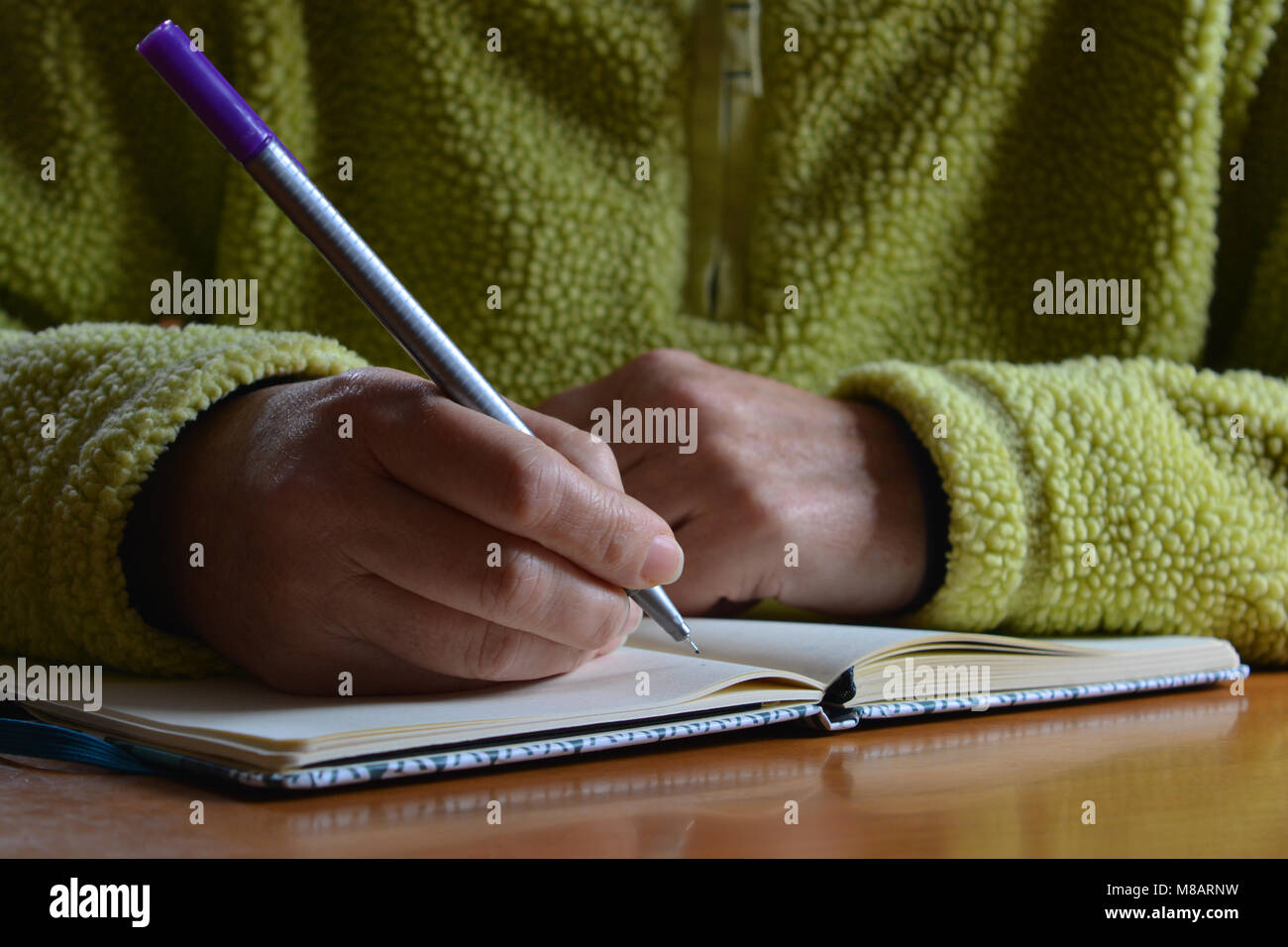 Femme assise à une table avec un stylo dans sa main, l'écriture sur un ordinateur portable Banque D'Images