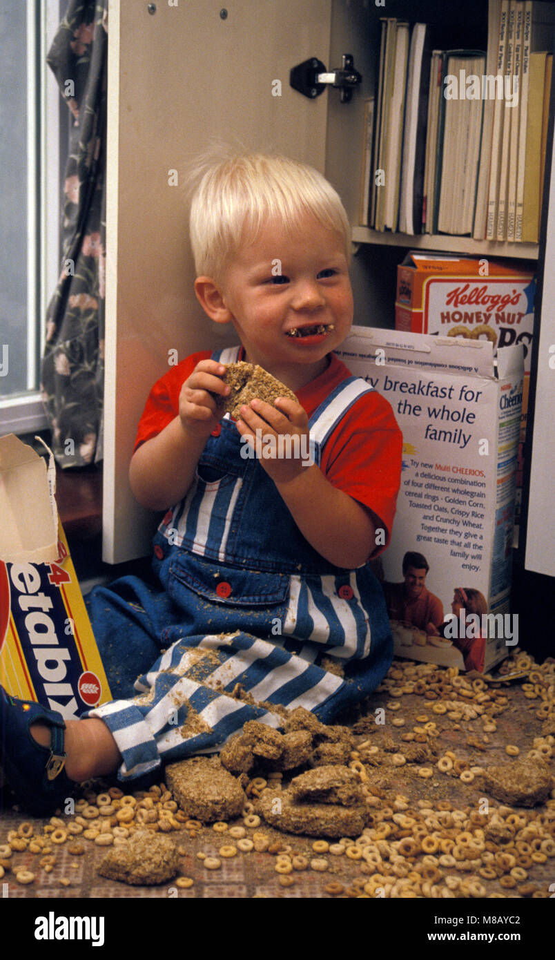 Enfant espiègle tipping hors des boîtes de céréales dans la cuisine Banque D'Images