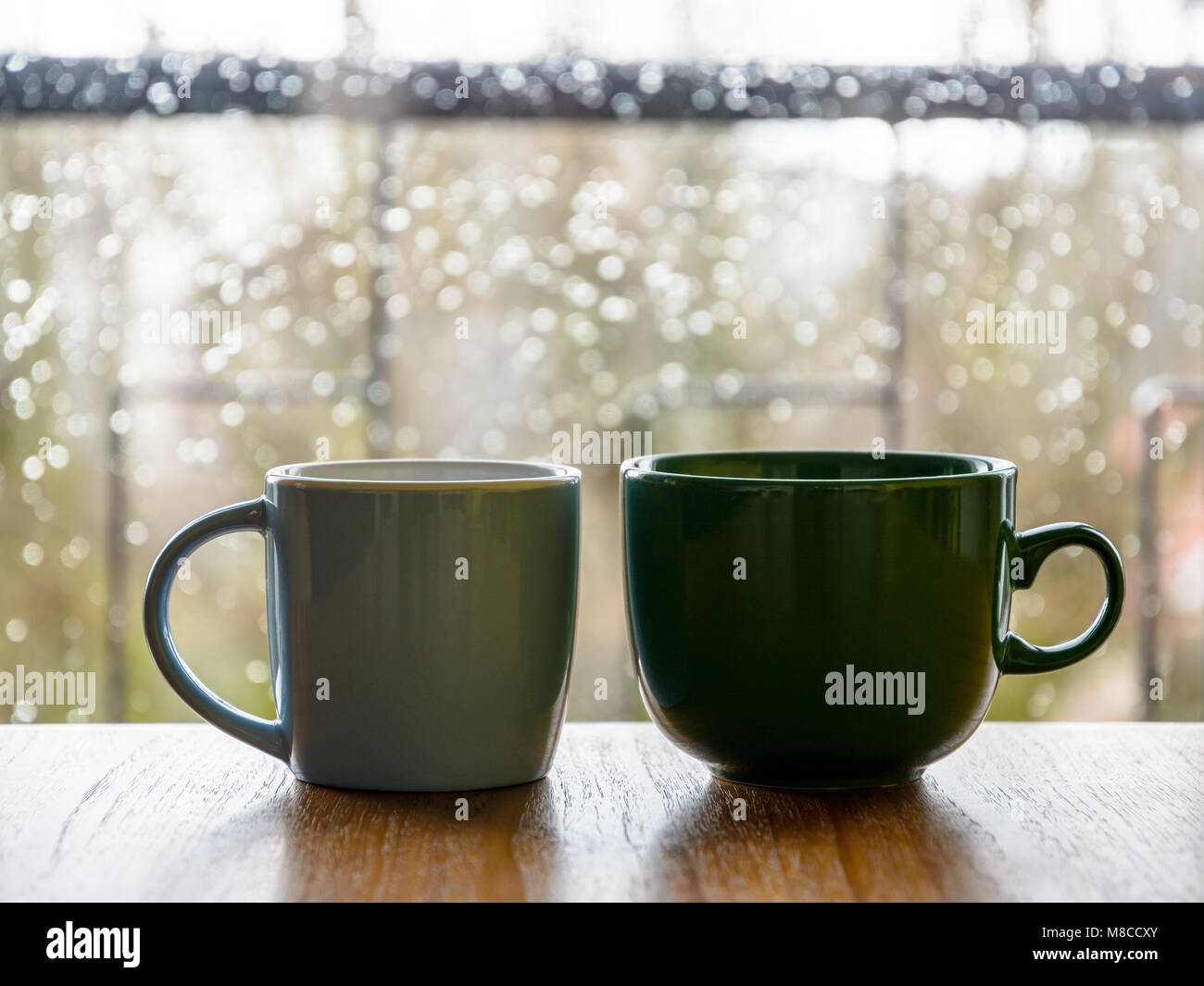 Deux mugs sur une table en bois en face d'une fenêtre en verre recouvert de gouttes de pluie. Banque D'Images