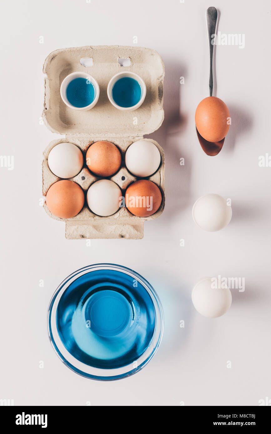 Vue de dessus de verre avec peinture bleu et l'autre les oeufs de poule sur la surface blanche, concept de Pâques Banque D'Images