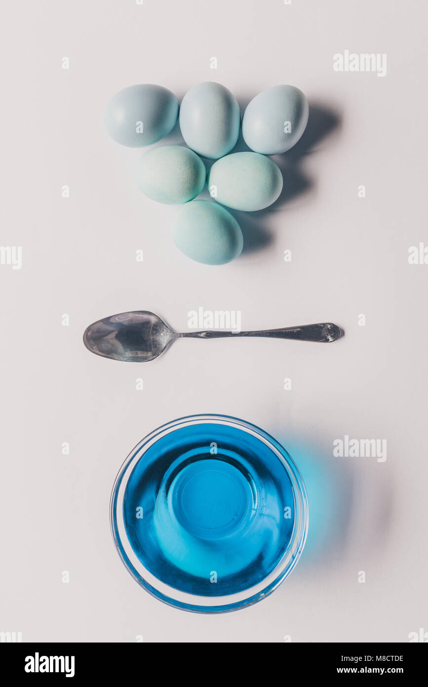 Vue de dessus de verre avec peinture bleue, une cuillère et les oeufs de poule sur la surface blanche, concept de Pâques Banque D'Images