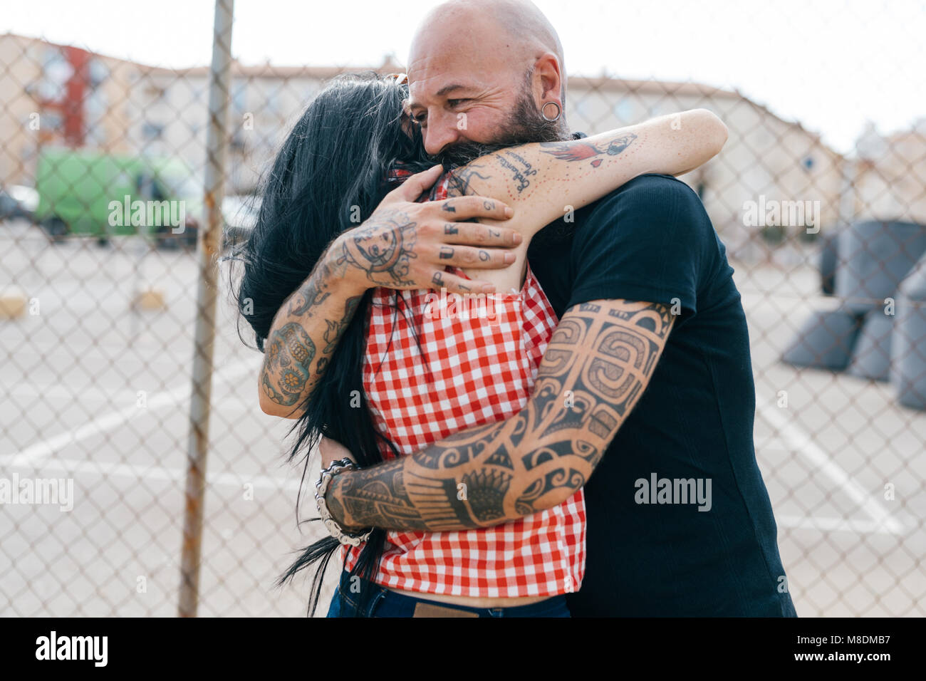 Hipster tatouée mature couple hugging by wire fence Banque D'Images