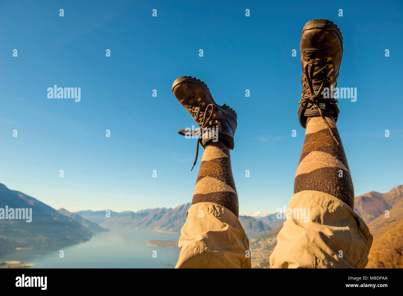 Des chaussures de randonnée et les jambes en l'air sur la chaîne de montagnes des Alpes et du Lac Majeur au Tessin, Suisse Banque D'Images